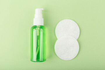 Close up of skin cleansing foam or gel next to two cotton pads on light green background