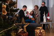 © Dani Palazón - Parents, daughter and grandparents at Christmas giving a gift to the baby with a Christmas tree in front