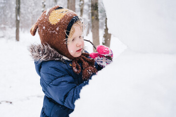 Children play outdoors in snow. Outdoor fun for family Christmas vacation. Two little kid boy and girl in funny hats playing outdoors. Happy siblings having fun with snowman