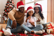 Black Family In Santa Claus Hats Putting Coin In Piggybank