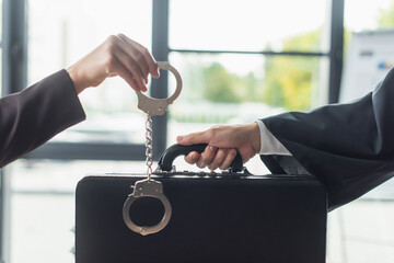 cropped view of woman holding handcuffs near man with briefcase, anti-corruption concept