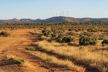 A Dry Dirt Track Leading Through Scrub Towards  Wind Turbines On Distant Hills