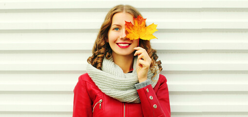 portrait of beautiful young woman covering her eyes with yellow maple leaves wearing a red jacket, s
