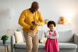 Glad happy african american small girl and old man dancing, have fun in living room interior