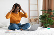 © Prostock-studio - Unhappy Black Woman Looking At Laptop Touching Head In Bedroom