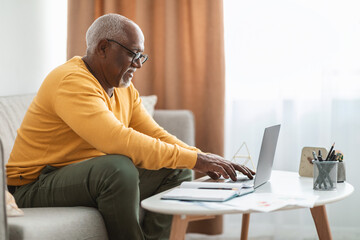 Wall Mural - Side-View Of Mature Black Man Typing On Laptop At Home