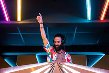 Bearded DJ Standing In Club With Outstretched Arm During Party