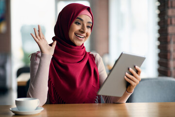 Wall Mural - Cheerful muslim woman in hijab having video chat, using tablet