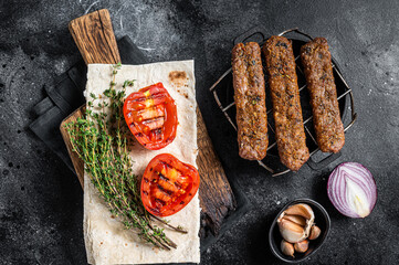 BBQ adana shish kebab on a grill with bread and tomato. Black background. top view