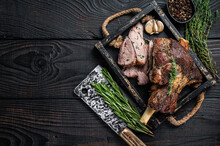 Roasted Mutton Lamb Leg Sliced In A Wooden Tray With Meat Cleaver. Black Wooden Background. Top View. Copy Space