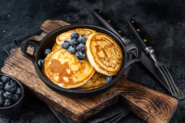 Pancakes with fresh blueberries and maple syrup in a pan. Black background. Top View