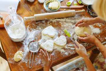 Cropped image of a female and kid hands holding dough in heart shape