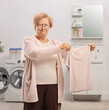 Grumpy elderly woman with a shrunken shirt in a bathroom