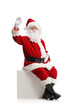 © Ljupco Smokovski - Santa claus sitting on a white cube and waving at camera