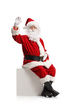 Santa Claus Sitting On A White Cube And Waving At Camera