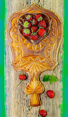 Wall Mural - Fresh red strawberries in a heart-shaped wooden plate on a carved wooden kitchen board, on a green background