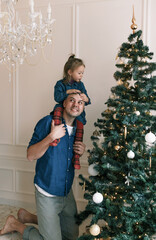 Wall Mural - a little daughter plays with her dad sitting on his shoulders while decorating a Christmas tree.