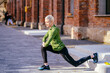 © Iryna - Middle age blond slim woman jogger in green activewear in an outdoor everyday sports routine. Female jogger workout, doing warming up exercise for legs.