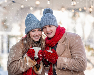 Cheerful young couple enjoying snow at backyard, drinking coffee