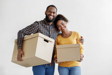 Satisfied young african american family carry cardboard boxes on white wall background in new home