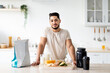 Portrait of handsome young Arab guy with healthy products and protein shake posing at kitchen