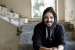 © Alex Sobrino - Portrait of a man with a hoodie smiling at camera in an abandoned warehouse