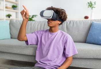 Canvas Print - Black teen guy wearing VR headset, exploring cyberspace, touching imaginary screen at home