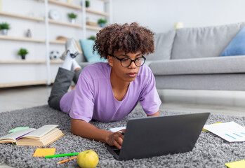 Poster - Focused black teenager using laptop pc for remote education, lying on floor and typing on keyboard at home