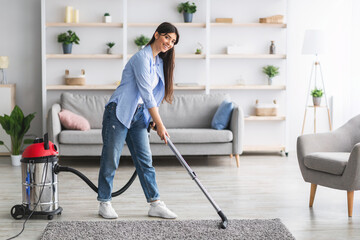 Wall Mural - Cheerful lady cleaning rug carpet with vacuum cleaner