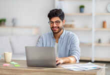 Portrait Of Happy Arab Freelancer Man Sitting At Desk With Laptop Computer At Home Office, Looking And Smiling At Screen
