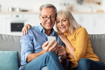 Happy Senior Couple Using Smartphone Together Sitting At Home