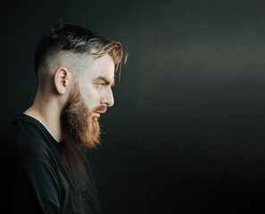 Cinematic portrait side view of a young hipster bearded man with copy space with cinematic lighting. Attractive man looking serious straight to camera, mental health concept. Depression and anxiety