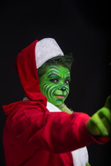 man dressed as christmas green, sitting in studio black background with santa claus suit