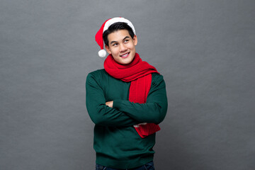 Young handsome Asian man in Christmas attire crossing arms and looking up in isolated gray color background