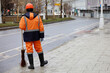 Janitor with broom in winter city, male municipal worker in uniform on sidewalk. Street cleaning, concept of unskilled labor