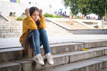 A sad teenage girl sits on the stairs and covers her head with her hands