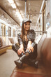 © Svyatoslav Lypynskyy - Smiling beautiful brunette female in modern latex clothes sits with folded legs on the seat in the empty metro car. Nice woman inside the night underground. Close-up Portrait. Toned picture