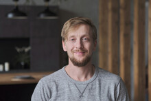 Portrait Confident Handsome European Bearded Man With Green Eyes Focused Face Expression Standing At Loft Kitchen. Stylish Blonde Male With Trendy Hairstyle Having Calmness Emotion Posing At Apartment