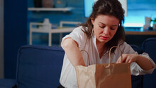 Young Adult With Face Mask Getting Meal Delivered At Home In Living Room Preparing To Eat Delicious Takeaway Food. Woman Feeling Hungry After Work, Having Takeout Order On White Table
