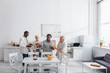 © LIGHTFIELD STUDIOS - Positive interracial elderly people holding tea and smartphone in nursing home