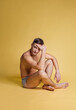 © master1305 - One young handsome shirtless brown-eyed man sitting on floor isolated on yellow studio background. Natural beauty concept