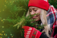 A Girl In A Red Knitted Hat With A Pumpon And Gloves Is Sitting In A Green Christmas Tree And Smiling With Her Mouth Wide Open With Teeth