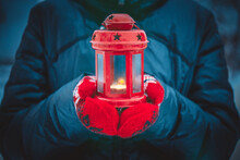 Man Holding A Red Candle Lantern With A Candle Close Up. A Man Dressed In A Warm Coat And Red Gloves