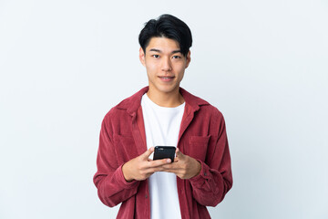 Poster - Young Chinese man isolated on white background looking at the camera and smiling while using the mobile