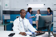 © DC Studio - African american pediatrician doctor working at healthcare treatment in hospital office typing medical expertise on computer during clinical examination. In background nurse examining patient