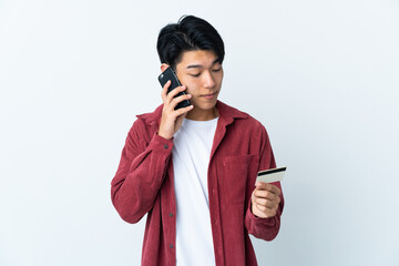 Poster - Young Chinese man isolated on white background buying with the mobile with a credit card