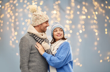 Sticker - people and winter holidays concept - happy couple in knitted hats and scarves over christmas lights background