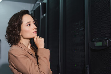 thoughtful woman looking at server while working in data center
