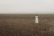 © Milou Dirks - Fine art portrait of woman in white dress standing alone in bare field on misty cold day