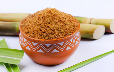 Wall Mural - Jaggery powder and sugarcane isolated on white background. Jaggery is used as an ingredient in sweet and savoury dishes in the cuisines of India. Selective focus.